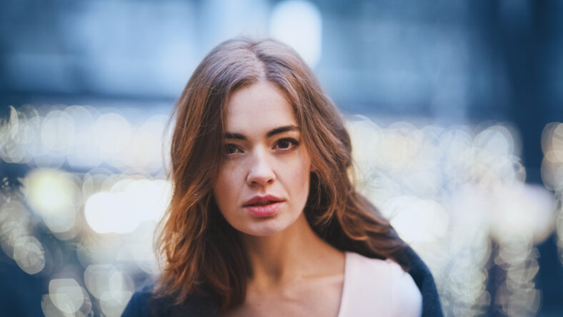 Attractive charming young woman in the holiday park. Blue trendy color ackground. Blurry lights. The holiday mood.