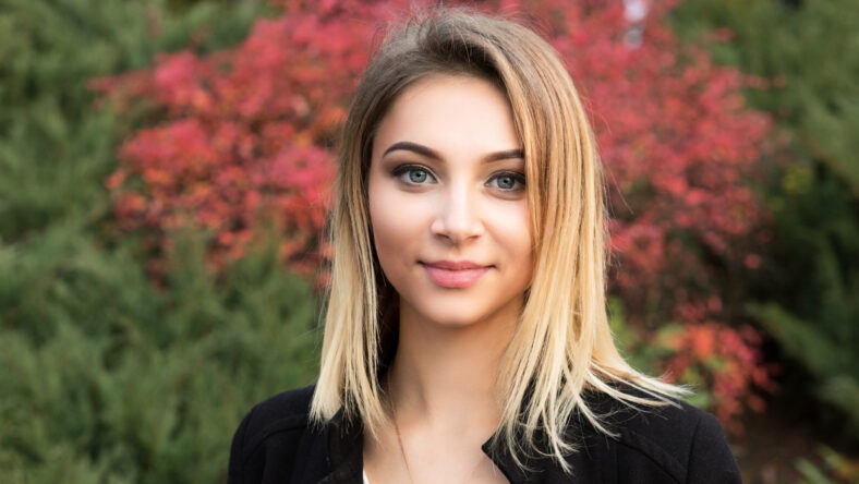 Portrait closeup of nice young woman against background of summer early autumn nature park green red leaves beautiful woman