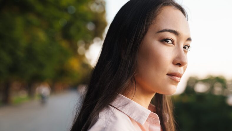 Image of pleased asian beautiful girl looking aside while walking in summer park