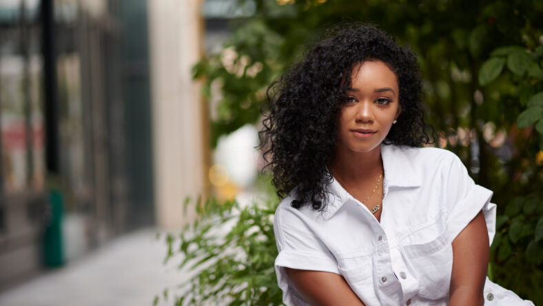 Stunning young black woman poses on city sidewalk wearing white romper in summer
