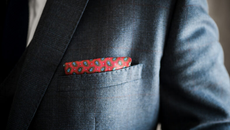 Elegant and stylish close up of silk pocket accessory handkerchief in Burgundy red with blue pattern tucked into wedding suit jacket pocket of groom on gentleman's wedding day