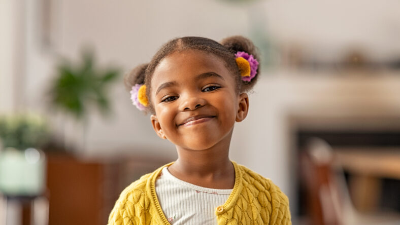 Smiling cute little african american girl with two pony tails looking at camera. Portrait of happy female child at home. Smiling face a of black 4 year old girl looking at camera with afro puff hair.
