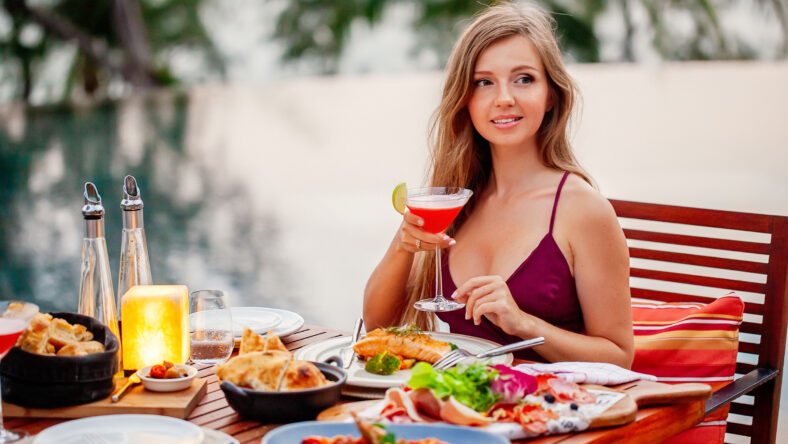 Elegant attractive smiling woman on romantic dinner in luxury gourmet restaurant. Happy young lady with a glass of cocktail in fine dining outdoor restaurant. Sexy elegant girl celebrating holiday.