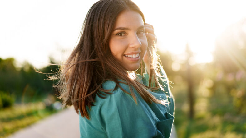 Portrait of young woman in green shirt smiling in a park, close up