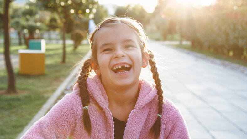 portrait of a laughing funny cheerful girl 6 years old in the park at sunset, missing front tooth