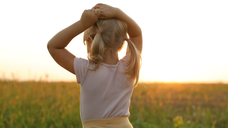 Cute little girl at meadow, back view. Child enjoying beautiful nature