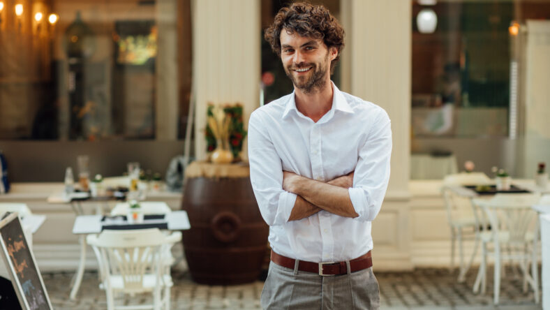 cheerful elegant man, standing outside in the street in front of his restaurant
