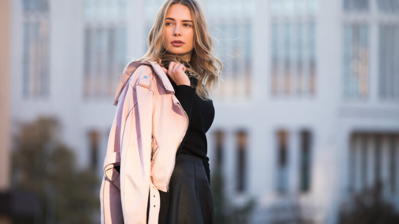 Autumn fashion. Stylish woman keeps her jacket over shoulder standing against european building background.