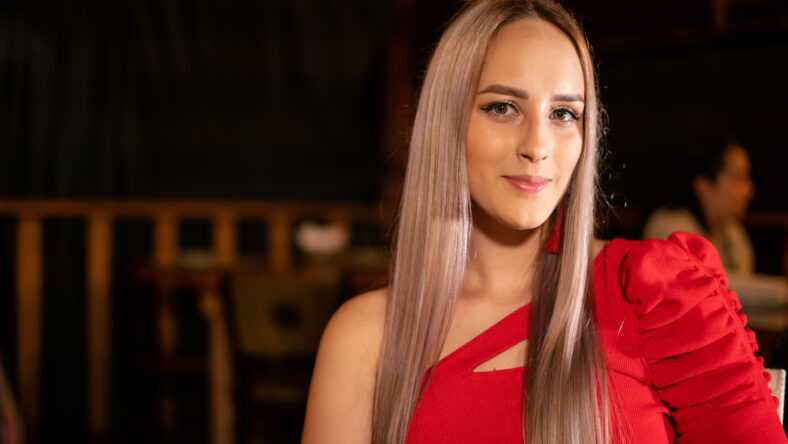 Young woman in red dress smiling at camera while sitting in cozy restaurant