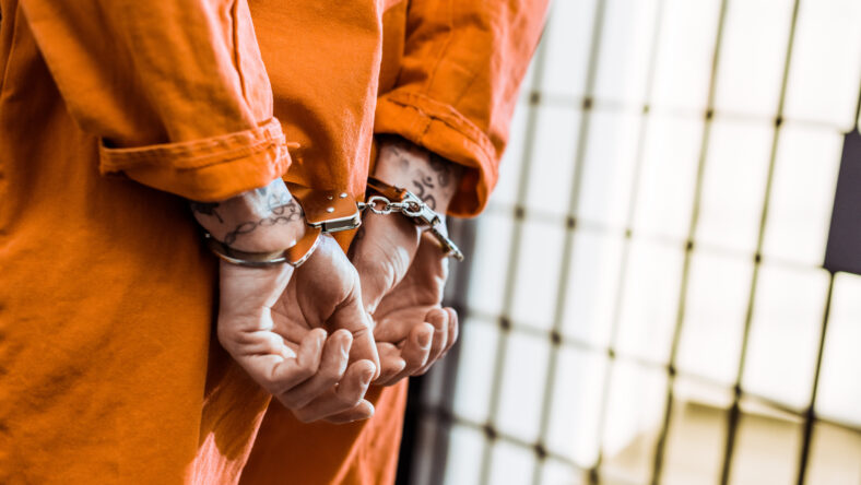 cropped image of tattooed prisoner standing in handcuffs in corridor