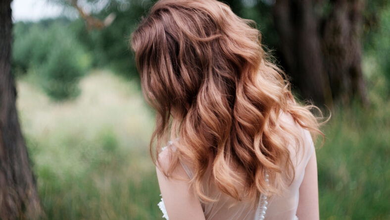 young pretty bride with curls n white wedding dress outdoors, view from behind