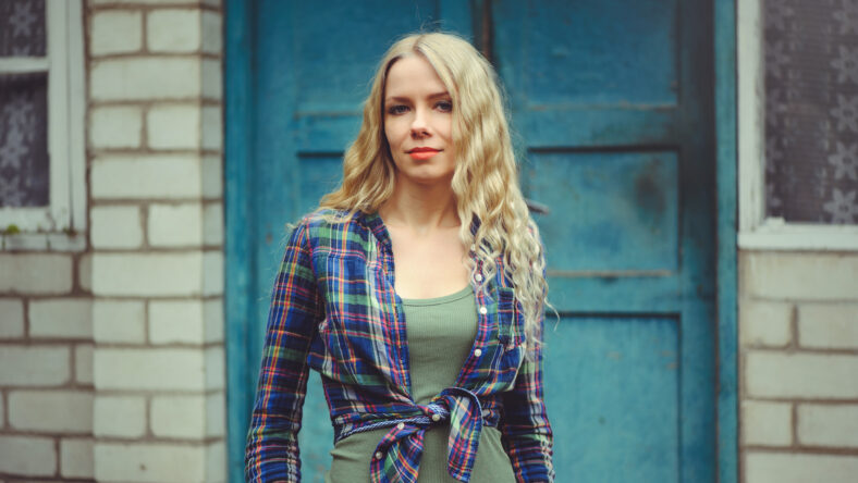attractive blonde girl on the background of an old house, dressed in jeans and shirts.