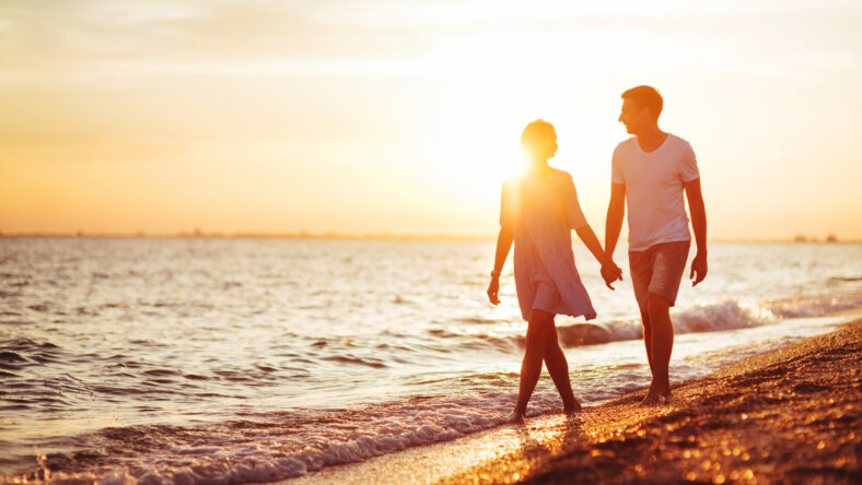 Young happy couple on seashore in the lights of sunset.