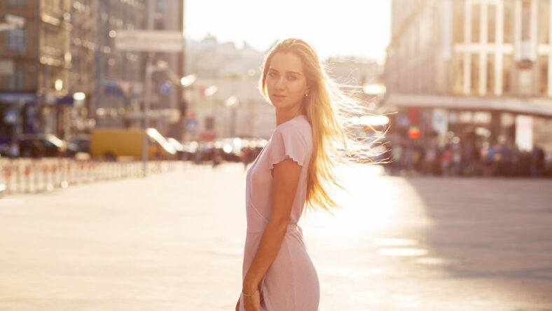 Wonderful blonde woman with flying hair posing at the street in sun beam. Female fashion concept. Empty space