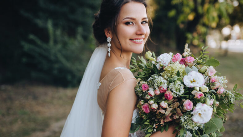 A beautiful bride stands on nature in greenery with a large bouquet. Wedding portrait close-up of the young bride. Wedding photography.