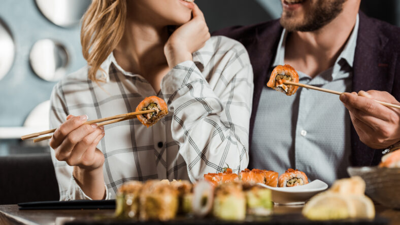 Cropped view of smiling happy couple eating sushi in restaurant
