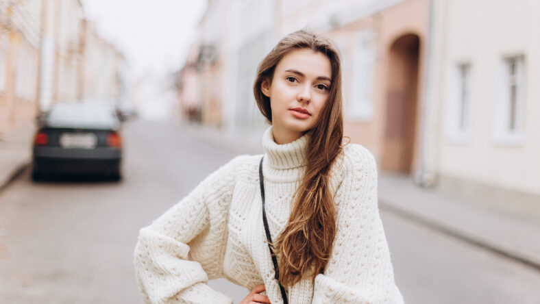 Portrait of young tender redhead young girl with healthy freckled skin wearing knitted scarf looking at camera with serious,pensive expression. Caucasian teen model with ginger hair posing outdoors