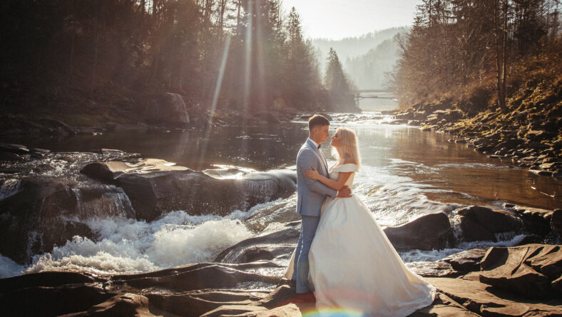 Amazing wedding couple, bride and groom holding hands on a mountains and rivers background. Cute girl in white dress, men in business suit. mountains landscape in the sunset. Concept of family.