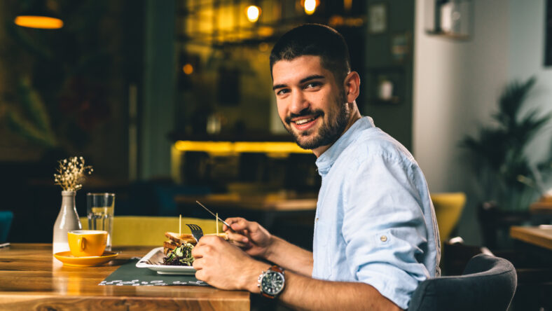 positive young man having breakfast or dinner in cafe