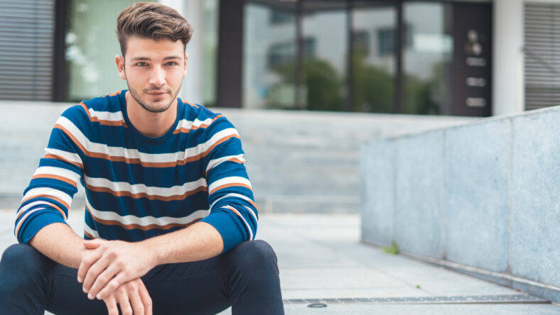 Handsome young man sitting on stairs, copy space
