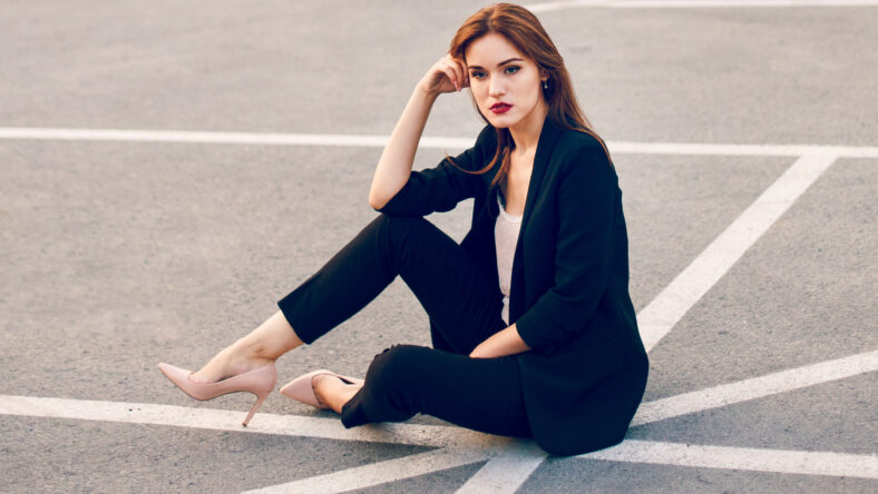 Red-haired model in a suit sits in a parking lot in summer