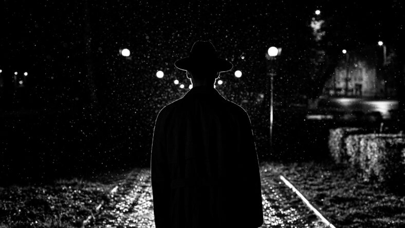 dark silhouette of a man in a hat in the rain on a night street in a city in the style of Noir