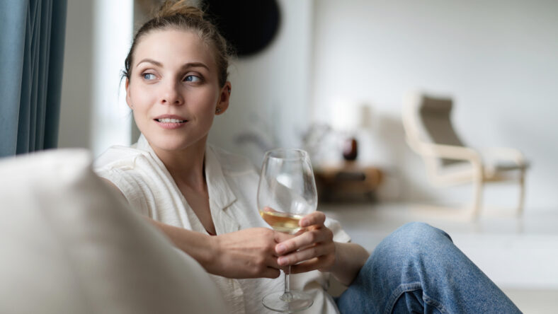 Successful young beautiful woman sitting on a sofa in the living room, drinking wine.