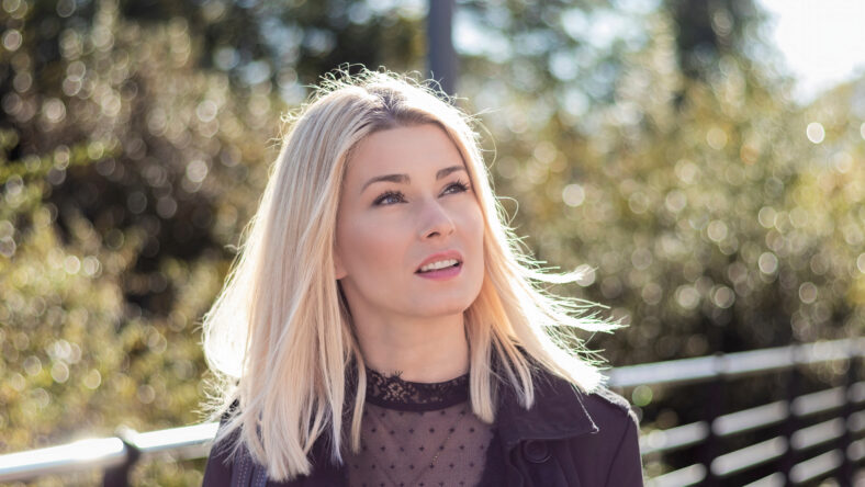 Confident blonde walking on a bridge one sunny day dressed in black