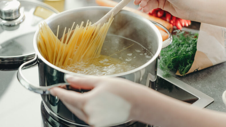 Girl cooking pasta in the kitchen, bowling pasta in pot.