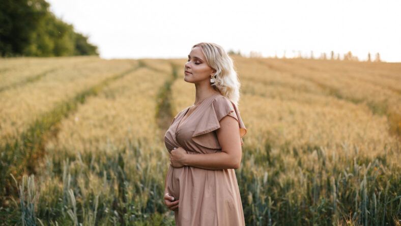 pregnant blonde woman in a field wearing a pink dress