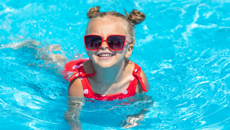 Child in swimming pool. Tropical vacation for family with kids. Little girl wearing red swimsuit playing in outdoor pool of exotic island resort. Water and swim fun for children