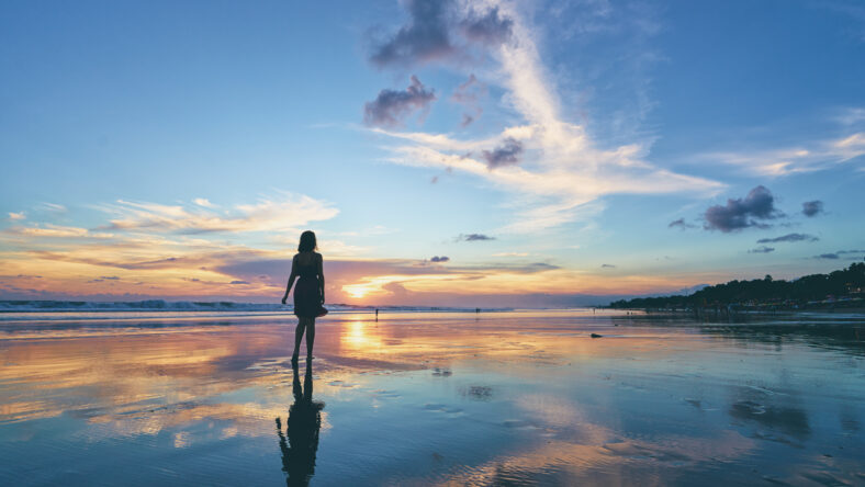 Sky and sea. Beautiful sunset. Silhouette of young woman walking on ocean beach.