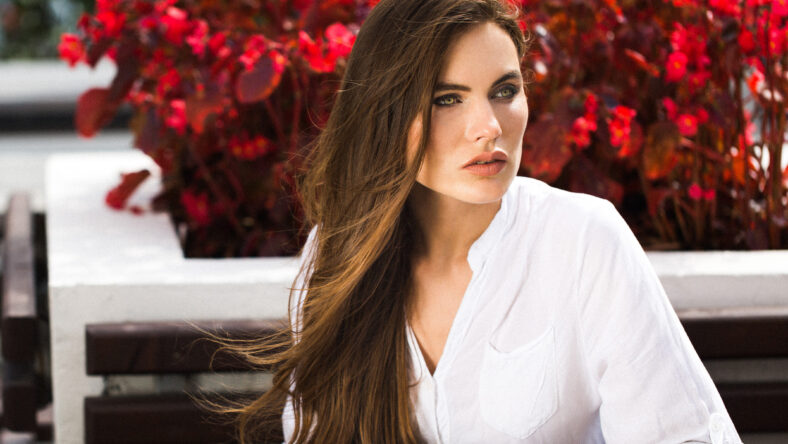 Stunning green-eyed woman sits before red flowers