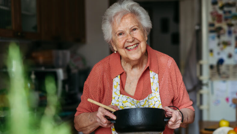 Happy senior woman cooking at home in kitchen.