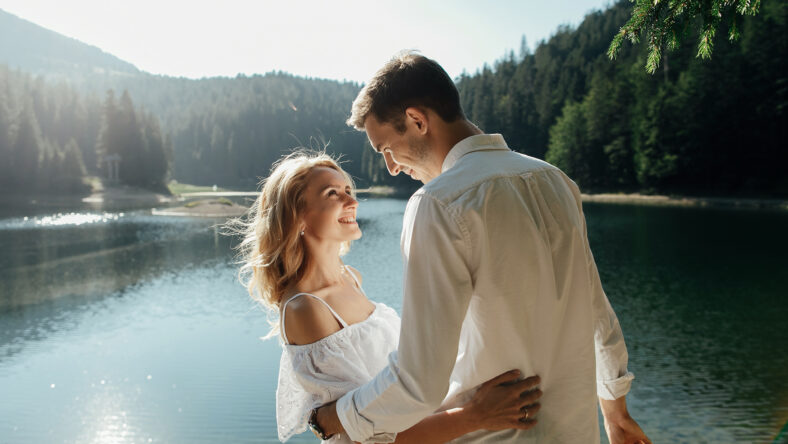 Young pretty couple hugging and smiling at the lake at sunset