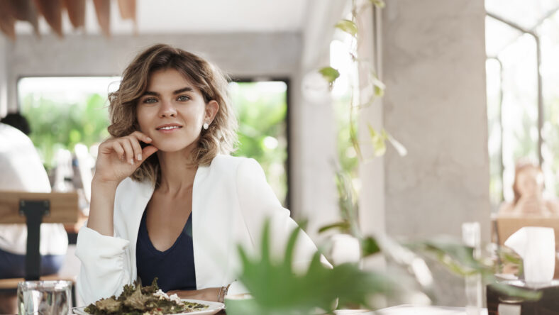 Stylush successful ambitious attractive young female marketing specialist sit restaurant modern cafe eat healthy salad drink coffee smiling delighted business meeting during lunch, discuss work.