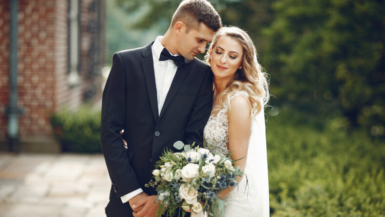 Beautiful bride in a long white dress. Handsome groom in a black suit. Couple in a summer park