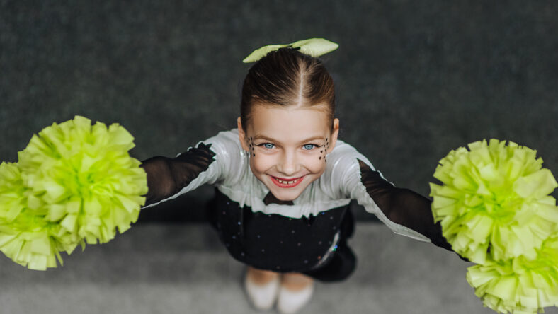 Beautiful happy girl athlete cheerleader in a costume with pompoms, a child of 8 years old with makeup, face painting, a champion rejoices at victory at a cheerleading competition. MyRealHoliday.
