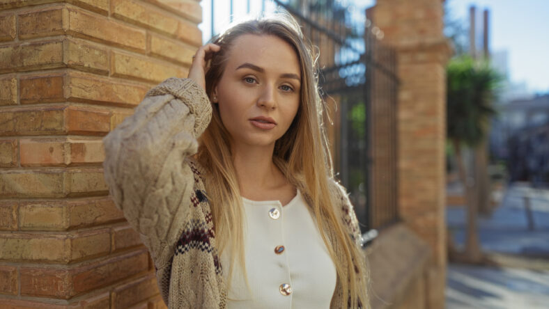 Woman standing confidently outdoors city street scene highlighting blonde hair wearing stylish casual clothing urban backdrop conveying youthful vibe sunny day