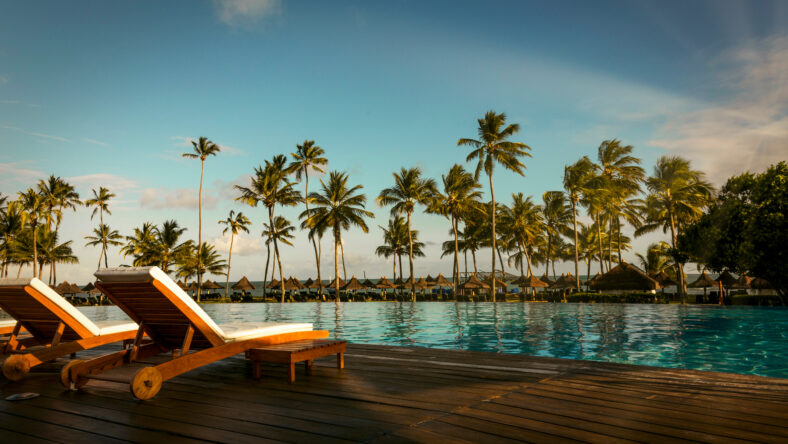 Beautiful tropical beach front hotel resort with swimming pool, sun-loungers and palm trees during a warm sunny day, paradise destination for vacations in Praia do forte, Bahia, Brazil.