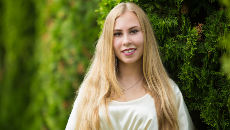 Portrait of a happy young pretty blonde girl in a dress between thuja on the street in autumn.