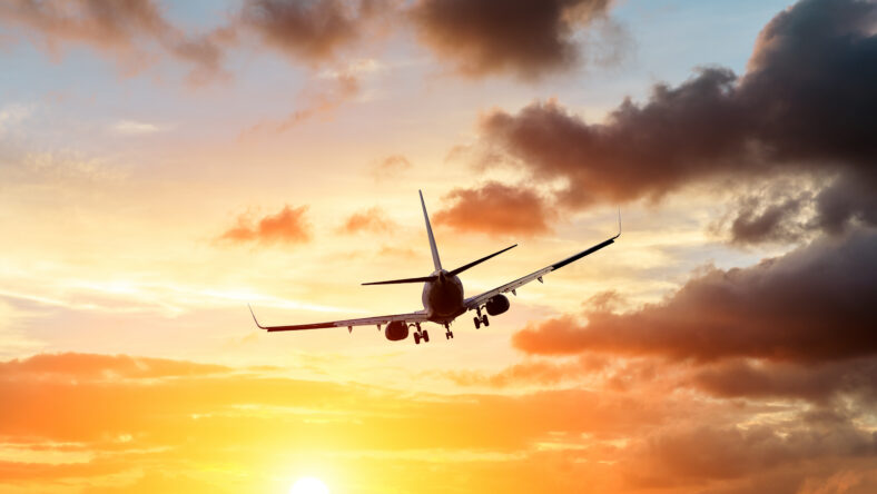 Commercial airplane flying above dramatic clouds during sunset