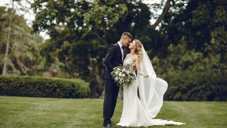Beautiful bride in a long white dress. Handsome groom in a black suit. Couple in a summer park