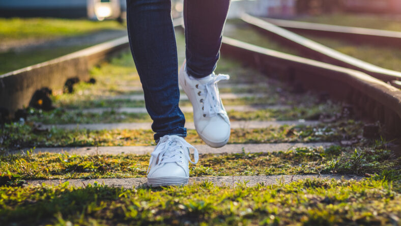 Woman wearing white sneakers running on railroad track