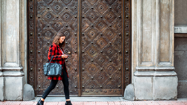 pretty young woman walking with black bag on the street talking via smartphone on autumn looking away