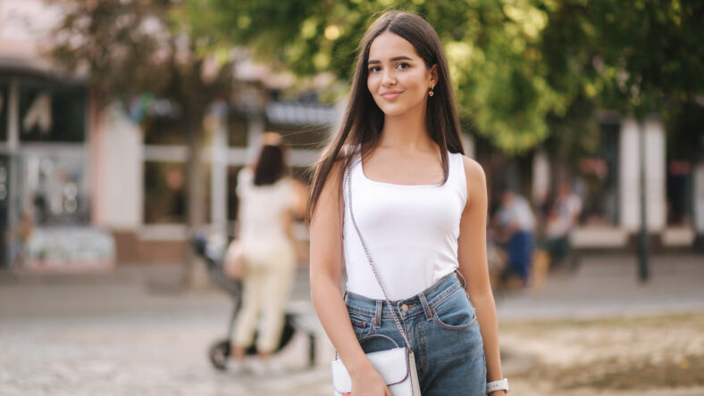 Attractive young woman walking in centre of city in summer time. Beautiful brunette in white shirt. Smile.