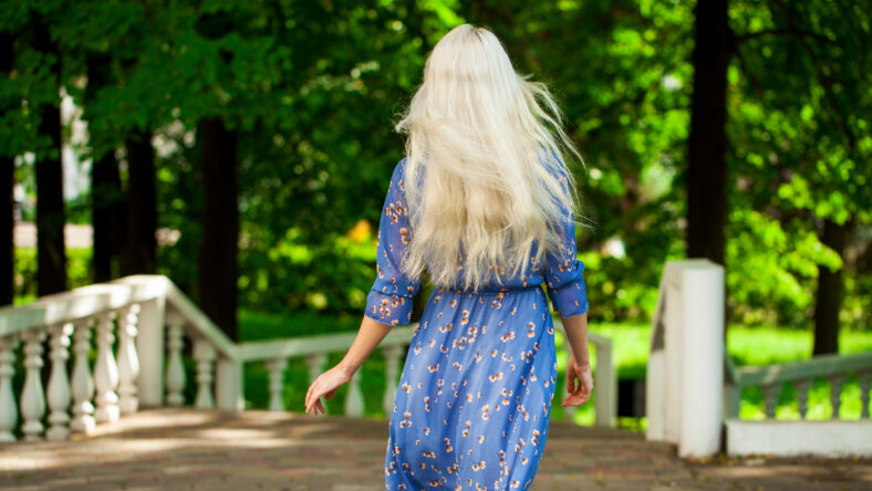 Portrait of a young beautiful blonde girl in blue flowers dress walking in summer park