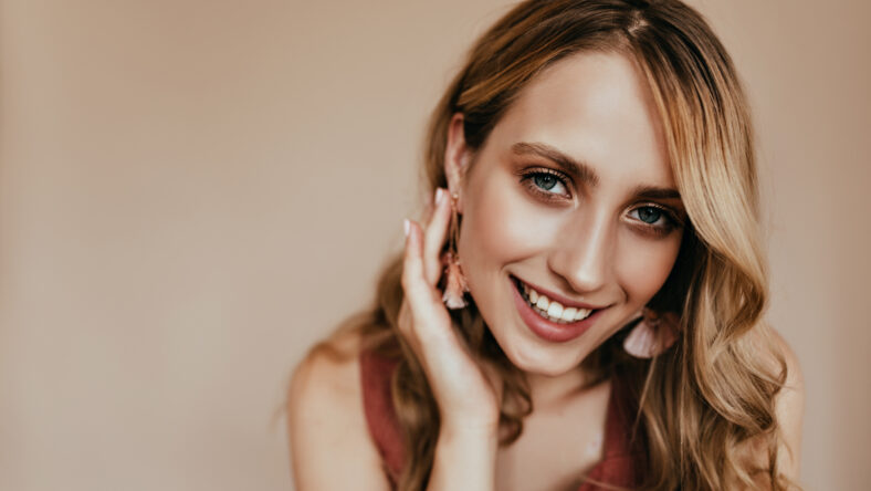 Joyful european woman gently touching her hair. Indoor photo of wonderful tanned caucasian girl posing on light background with smile.
