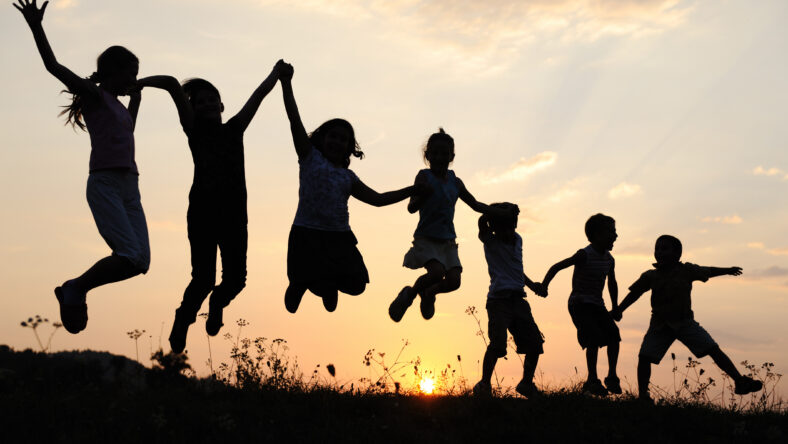 Silhouette, group of happy children playing on meadow, sunset, summertime