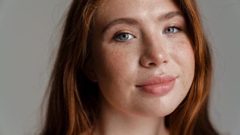 Portrait of a smiling young curvy young white woman with long red hair standing over wall background